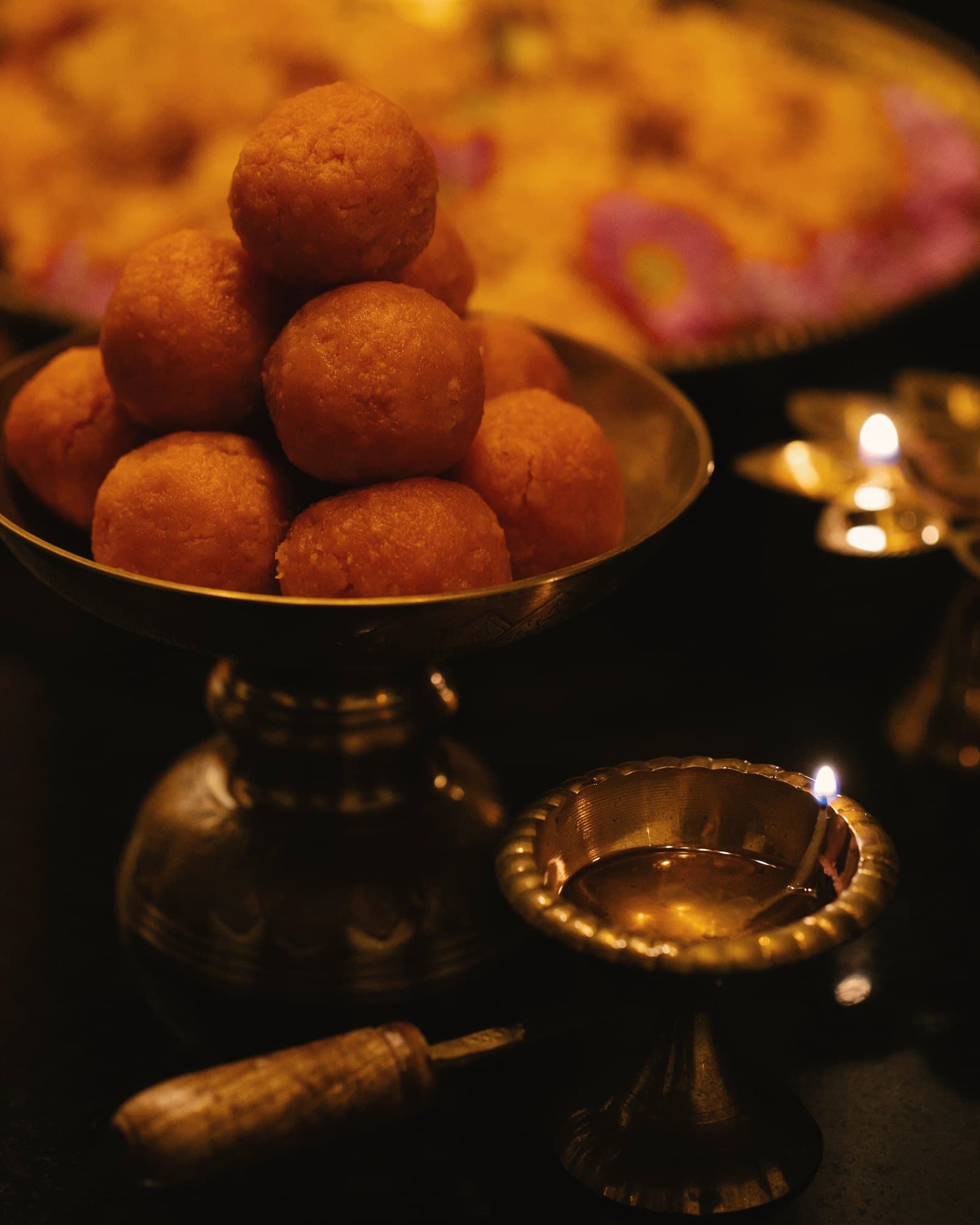 Brass bowl of laddoos with lit brass diyas
